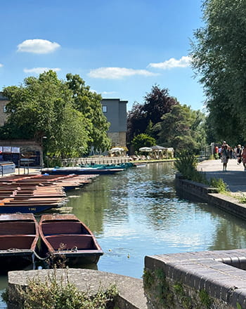 A canal with boats and people walking on the path by the river